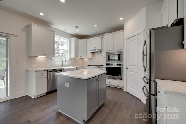kitchen with a center island, under cabinet range hood, a sink, backsplash, and stainless steel appliances
