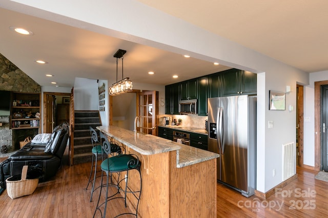kitchen featuring appliances with stainless steel finishes, light wood finished floors, light stone countertops, a kitchen bar, and green cabinets