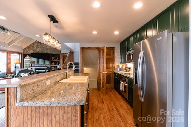 kitchen with stainless steel appliances, green cabinets, a sink, light wood-type flooring, and light stone countertops