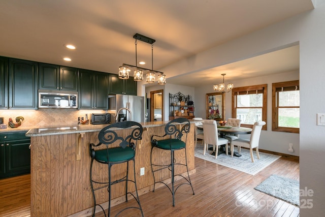 kitchen featuring appliances with stainless steel finishes, a chandelier, backsplash, a kitchen breakfast bar, and light wood-style flooring