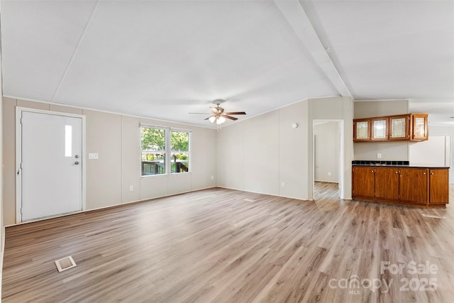 unfurnished living room with ceiling fan, lofted ceiling with beams, visible vents, and light wood-type flooring