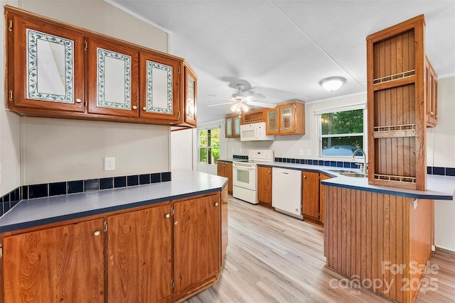 kitchen featuring brown cabinets, a sink, light wood finished floors, a peninsula, and white appliances