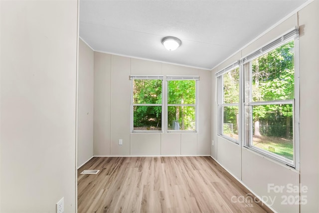 spare room featuring light wood-style floors, ornamental molding, vaulted ceiling, and visible vents