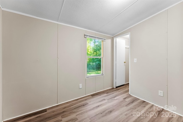empty room with light wood-style floors, ornamental molding, a textured ceiling, and lofted ceiling