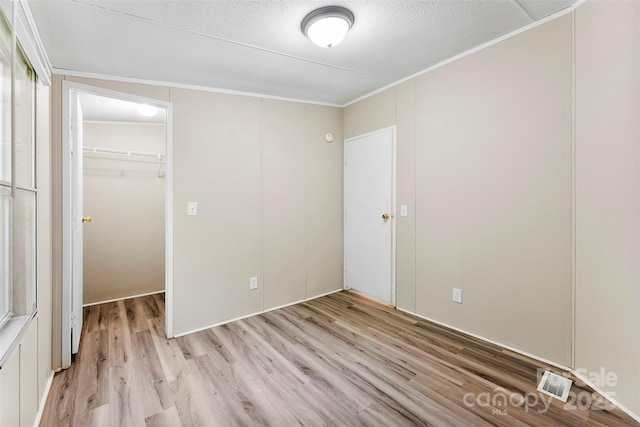unfurnished bedroom featuring crown molding, light wood finished floors, a spacious closet, visible vents, and a closet