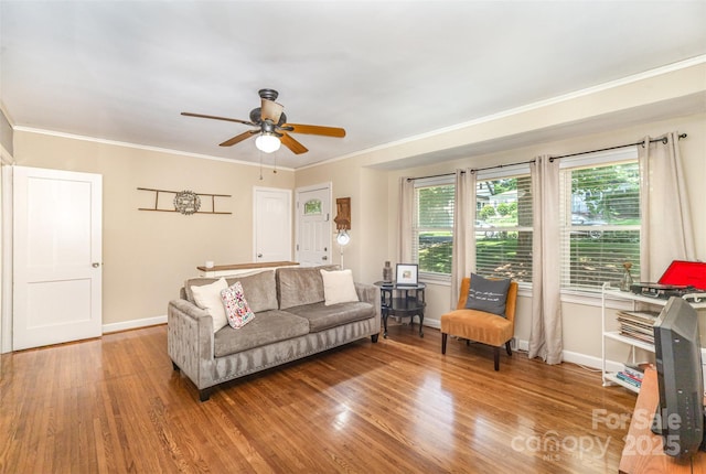 living area with wood finished floors, a ceiling fan, baseboards, and crown molding