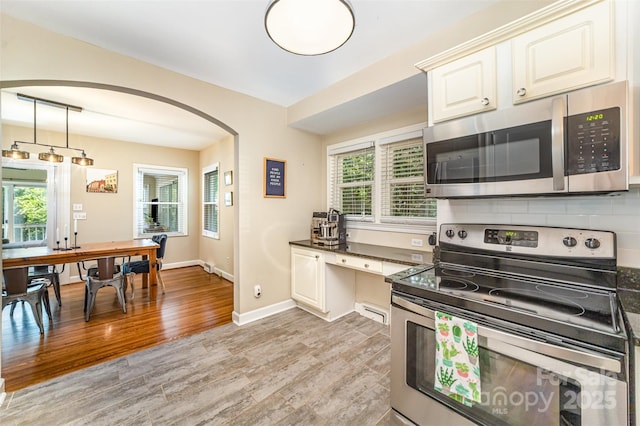 kitchen featuring stainless steel appliances, arched walkways, light wood-type flooring, dark countertops, and hanging light fixtures