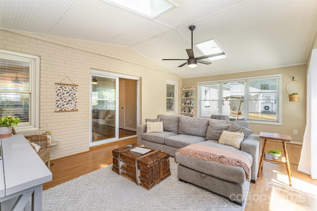 living area with a skylight, brick wall, wood finished floors, a ceiling fan, and vaulted ceiling