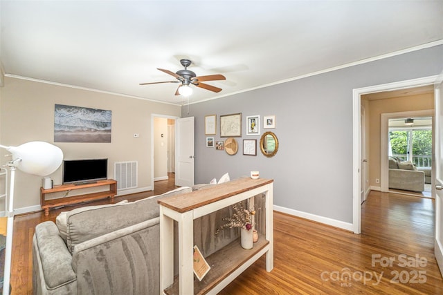 living room with a ceiling fan, ornamental molding, baseboards, and wood finished floors