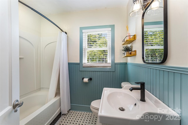 bathroom with a wainscoted wall, healthy amount of natural light, toilet, a sink, and shower / bath combo with shower curtain