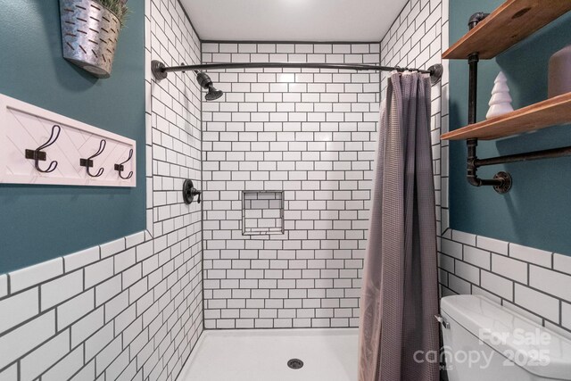 full bathroom with tile walls, a shower stall, toilet, and a wainscoted wall