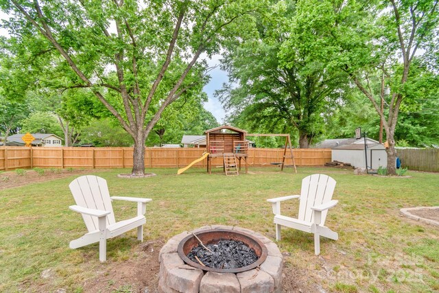 view of yard with a fire pit, a playground, a storage unit, and an outbuilding