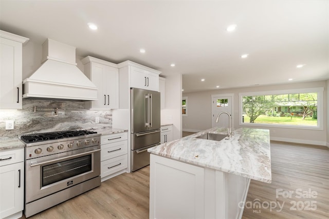 kitchen with a sink, light wood finished floors, custom exhaust hood, and premium appliances