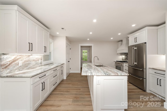 kitchen featuring high end appliances, tasteful backsplash, a sink, premium range hood, and recessed lighting