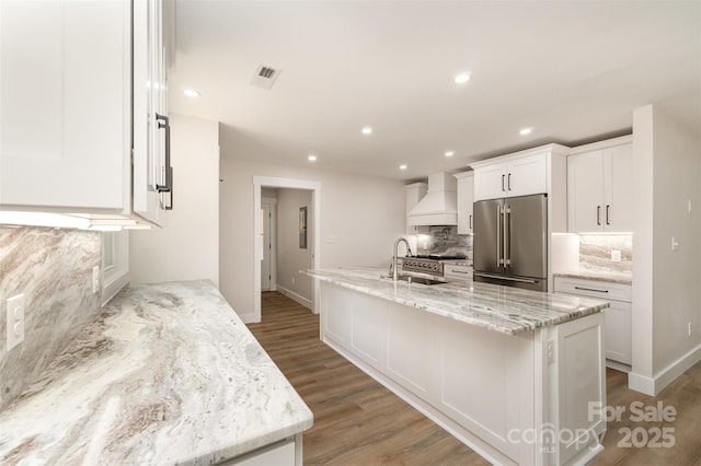 kitchen with backsplash, high quality fridge, a sink, premium range hood, and white cabinets