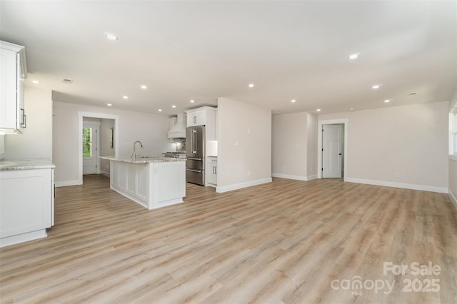unfurnished living room featuring recessed lighting, a sink, light wood-style flooring, and baseboards