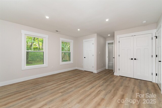 unfurnished bedroom featuring recessed lighting, baseboards, two closets, and light wood-style floors