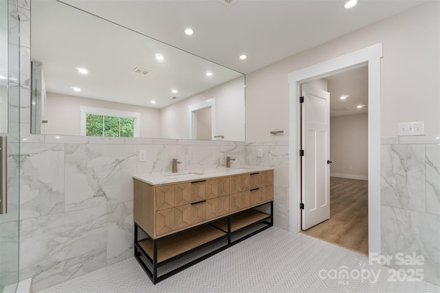 full bath featuring double vanity, a sink, tile walls, and wood finished floors