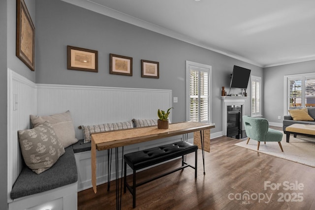dining area featuring wainscoting, ornamental molding, a fireplace with flush hearth, and wood finished floors