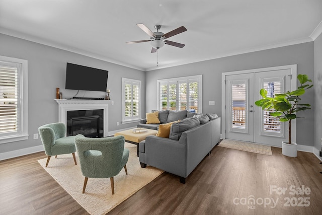 living area with french doors, crown molding, ceiling fan, a glass covered fireplace, and dark wood-style floors