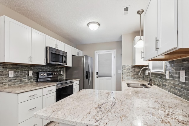 kitchen with stainless steel appliances, a sink, light stone countertops, white cabinets, and decorative backsplash