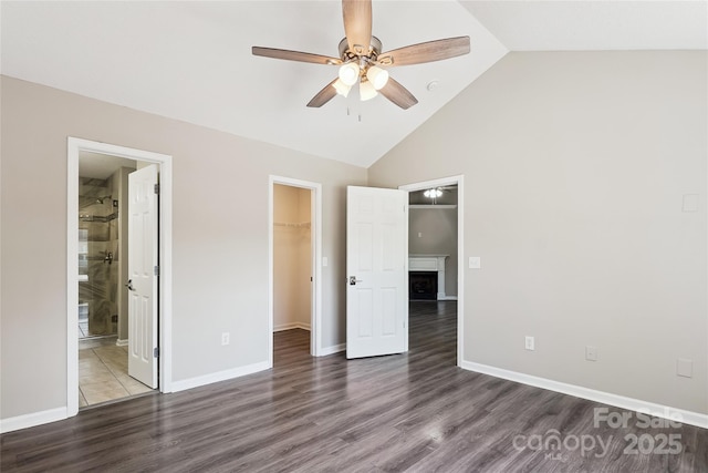 unfurnished bedroom featuring a fireplace, a walk in closet, a closet, and wood finished floors