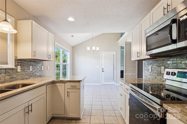 kitchen with appliances with stainless steel finishes, vaulted ceiling, backsplash, a chandelier, and light tile patterned flooring