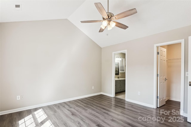 unfurnished bedroom with lofted ceiling, a walk in closet, wood finished floors, and baseboards