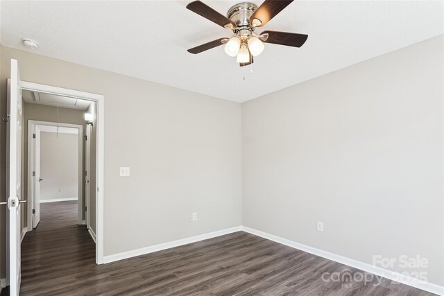 unfurnished room featuring attic access, dark wood-type flooring, baseboards, and a ceiling fan