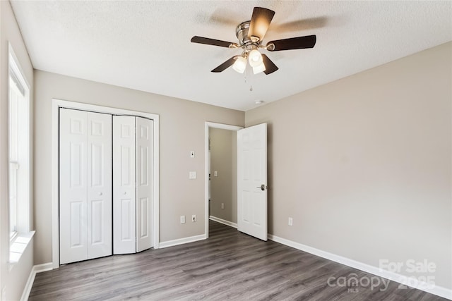 unfurnished bedroom featuring wood finished floors, a closet, multiple windows, baseboards, and a textured ceiling