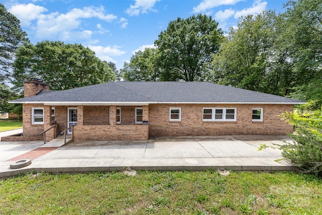 rear view of house featuring brick siding, a shingled roof, a chimney, and a patio