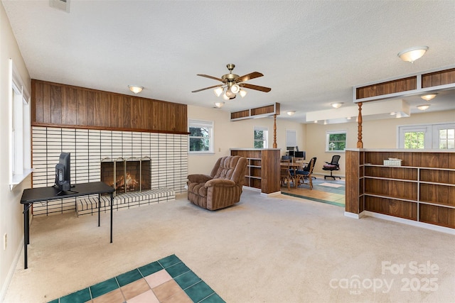 carpeted living area with ceiling fan and a lit fireplace