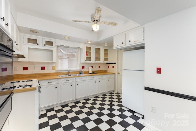 kitchen with a sink, light floors, tasteful backsplash, and freestanding refrigerator