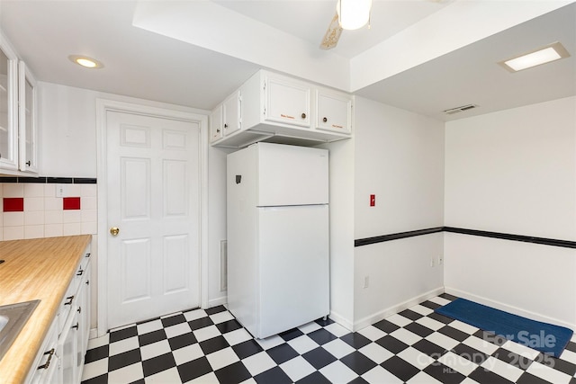 kitchen with white cabinets, dark floors, wood counters, freestanding refrigerator, and visible vents