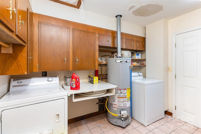 clothes washing area with cabinet space, washing machine and dryer, light tile patterned floors, and water heater