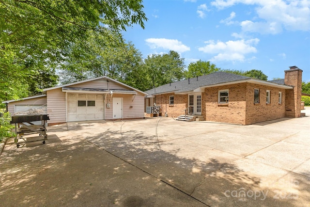 rear view of property with an outdoor structure, a garage, a chimney, brick siding, and central air condition unit