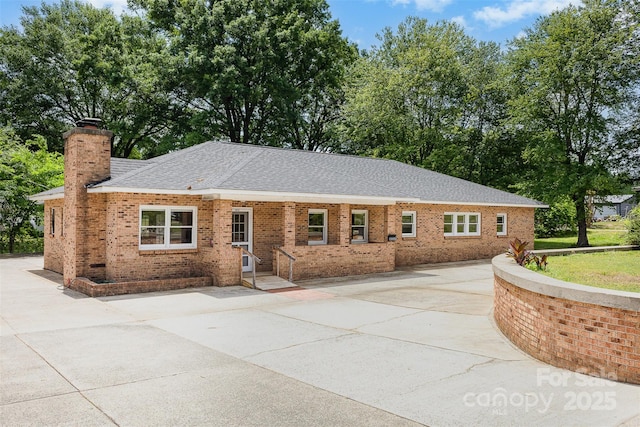 ranch-style home featuring brick siding, a chimney, and a shingled roof