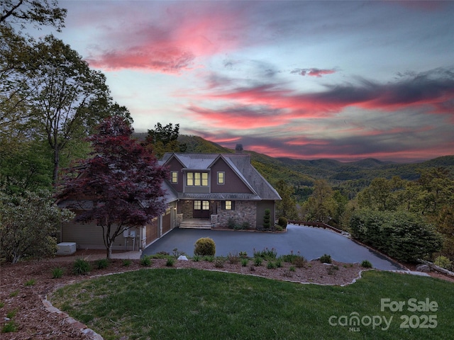 view of front of house featuring a front lawn, aphalt driveway, a garage, stone siding, and a chimney