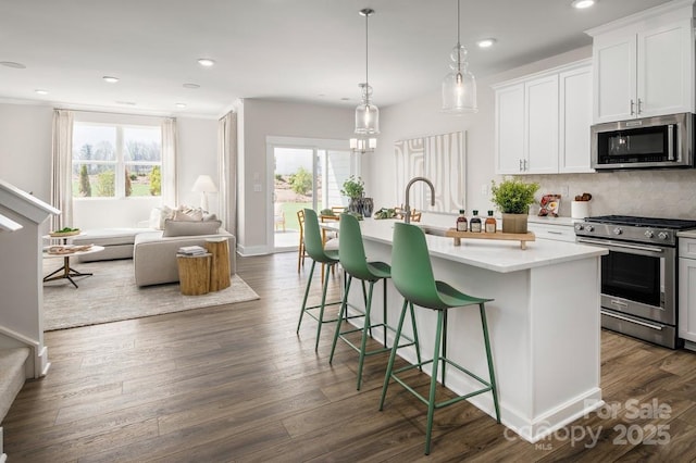 kitchen featuring stainless steel appliances, a sink, a kitchen island with sink, light countertops, and tasteful backsplash