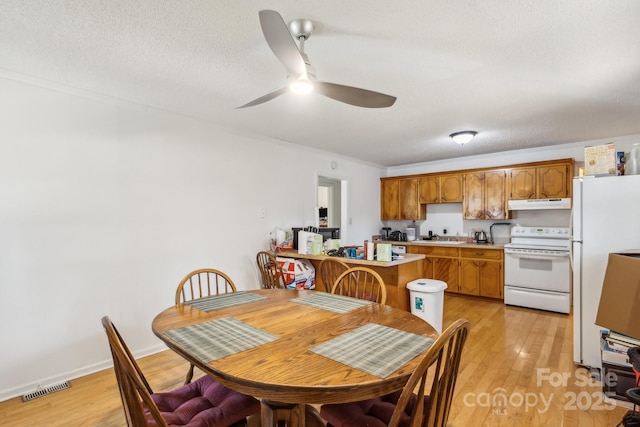 dining space featuring a ceiling fan, a textured ceiling, visible vents, and light wood finished floors