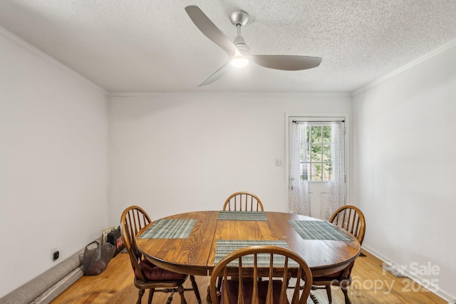 dining area featuring light wood-style floors, a ceiling fan, a textured ceiling, and crown molding