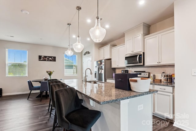 kitchen featuring an island with sink, backsplash, dark wood-type flooring, and appliances with stainless steel finishes
