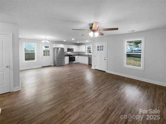 unfurnished living room with a healthy amount of sunlight, baseboards, and ceiling fan with notable chandelier
