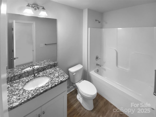 bathroom featuring wood finished floors, shower / washtub combination, vanity, baseboards, and toilet