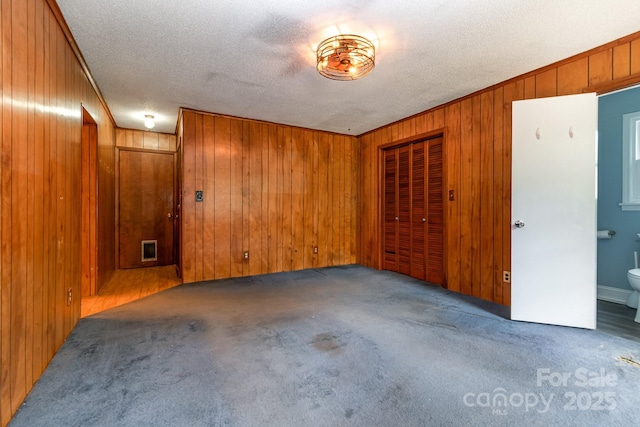 empty room with crown molding, carpet flooring, a textured ceiling, and wooden walls