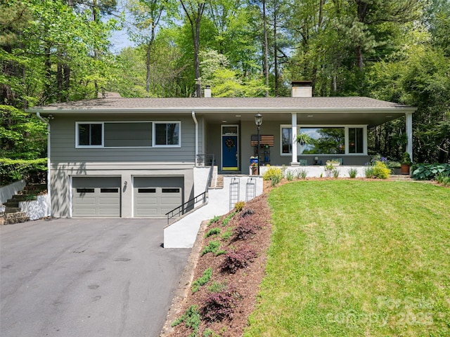view of front of property with a garage, covered porch, a front yard, a chimney, and driveway