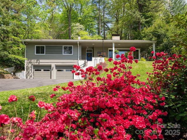 view of front facade with a front lawn, aphalt driveway, a garage, a chimney, and covered porch