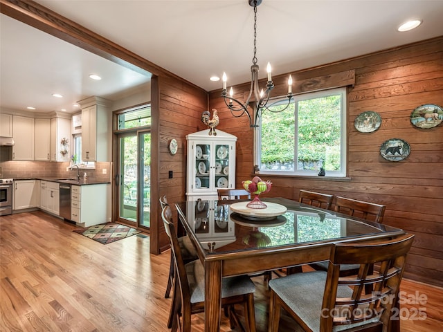 dining area with an inviting chandelier, wood walls, light wood-style flooring, and a wealth of natural light