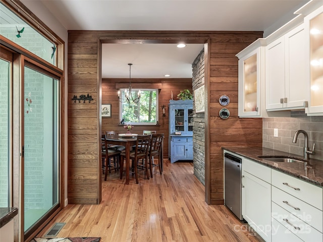 kitchen featuring white cabinets, a sink, wood walls, light wood-type flooring, and stainless steel dishwasher