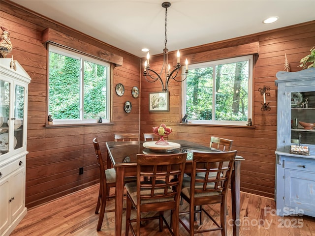 dining space featuring wooden walls, an inviting chandelier, plenty of natural light, and light wood finished floors